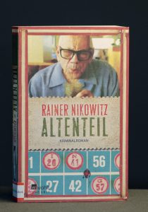 Książka Rainera Nikowitza "Altenteil". Na okładce wizerunek starszego mężczyzny pijącego sok przez słomkę.