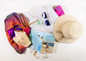 Zdjęcie zawartości plażowej torby: książki Wyspa, Victorii Hislop, kapelusza słomkowego, okularów przeciwsłonecznych, zielonych słuchawek dousznych, muszli i małych muszelek.