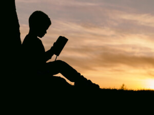 Zdjęcie kontur siedzącego i czytającego książkę dziecka na tle zachodzącego słońca.