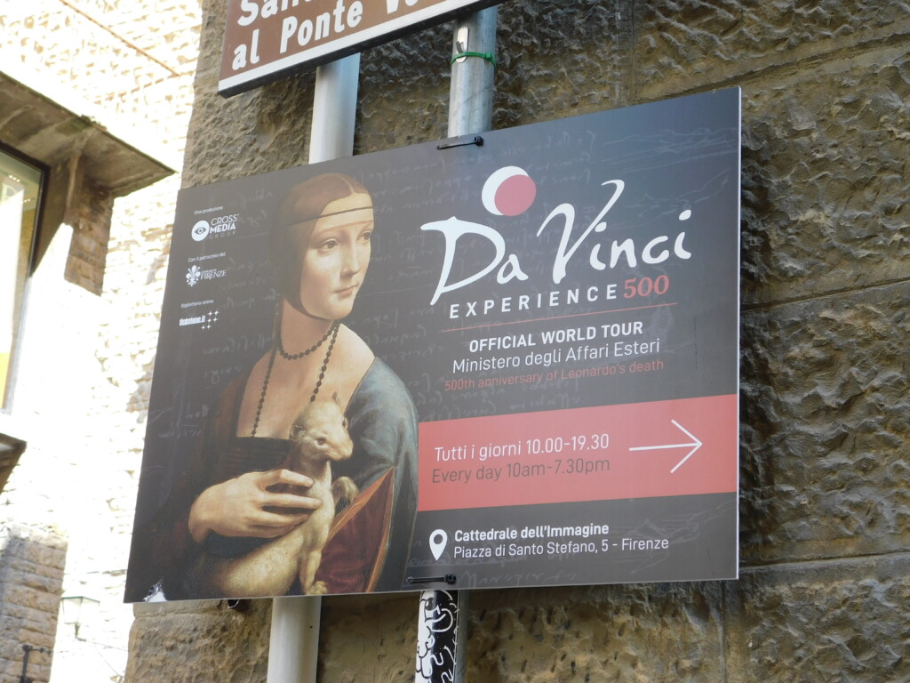 Zdjęcie plakatu przedstawiającego Damę z gronostajem. Plakat przymocowany na rurze przymocowanej do muru.