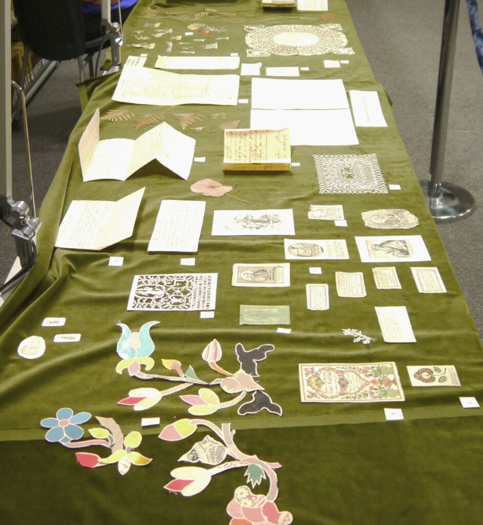 Stół nakryty zielonym płótnem. Na stole rozłożone pocztówki i odręcznie pisane kartki.