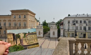 Zdjęcie, na pierwszym planie pocztówka z widokiem bramu Uniwersytetu Warszawskiego, w tle ta brama właśnie.