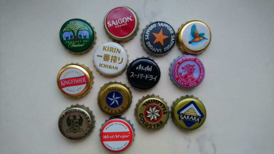 Zdjęcie kilkunastu różnokolorowych kapsli od piwa ułożonych na jasnym tle