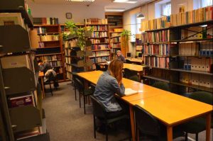 osoby uczące się przy stołach w czytelni bibliotecznej