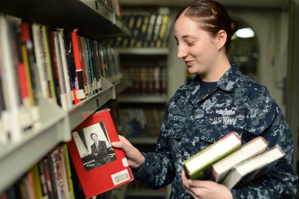 Marynarz ustawia książki w bibliotece okrętowej.