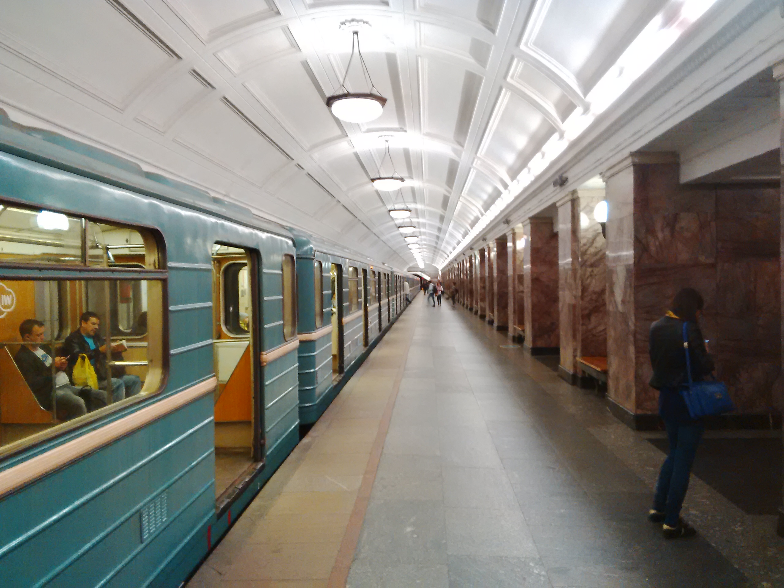 Widok stacji metra w Moskwie z niebieskim wagonikiem kolejki, marmurową posadzką i żyrandolami