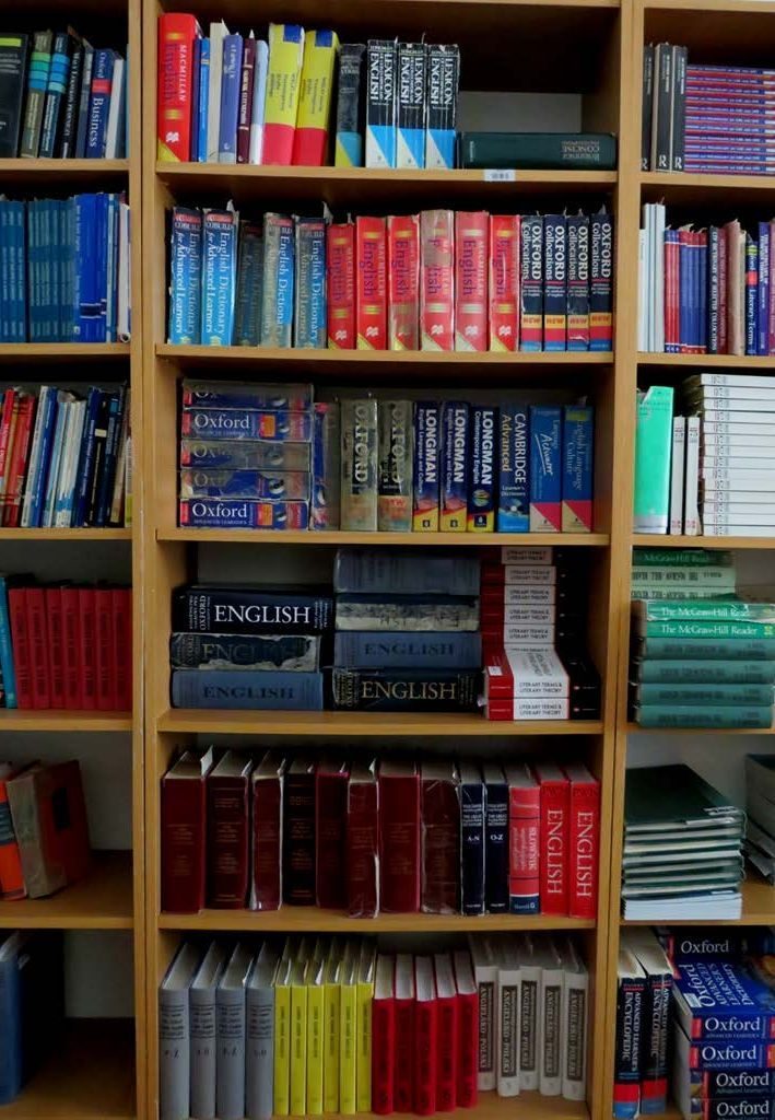 Zdjęcie drewnianego regału bibliotecznego zastawionego książkami noszącymi ślady zużycia.
