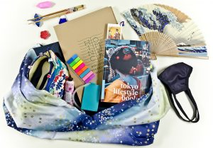 Zdjęcie kolorowej torby oraz jej zawartości: książki Tokyo lifestyle book, notatnika, wachlarza z orientalnym wzorem fal, pałeczek, opaski na oczy.
