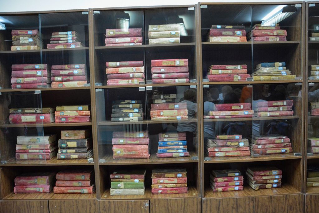 Zdjęcie oszklonych witryn regałów, w których są przechowywane oprawne tomy rękopisów.
