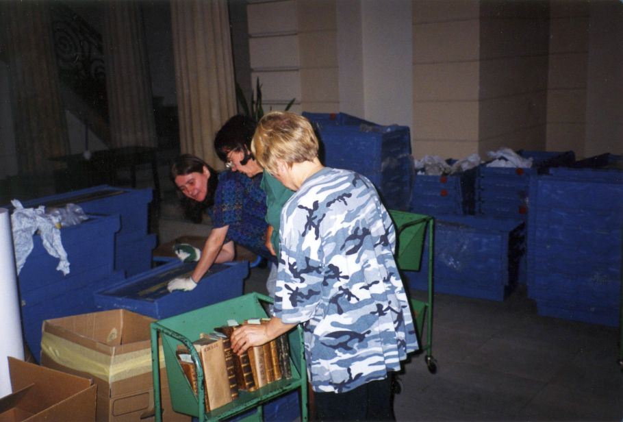 Zdjęcie trzech kobiet pakujących książki do kontenerów transportowych..