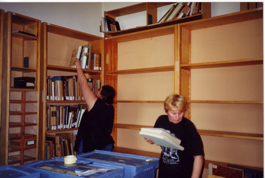 Zdjęcie dwóch Pań układających książki na drewnianych regałach w pracowni bibliotecznej.