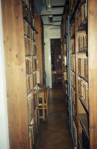 Zdjęcie przejścia między drewnianymi regałami zastawionymi książkami w magazynie bibliotecznym.