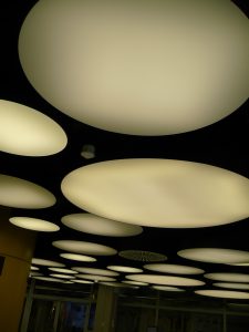 Zdjęcie nowoczesnych, okrągłych, mlecznobiałych lampo pod sufitem w holu biblioteki.