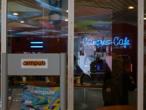 Zdjęcie drzwi wejściowych do kawiarni, z neonem: Campus-Cafe.