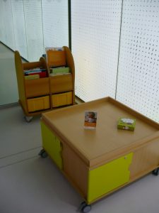Zdjęcie drewnianego stolika oraz wózka bibliotecznego z książkami dla dzieci.