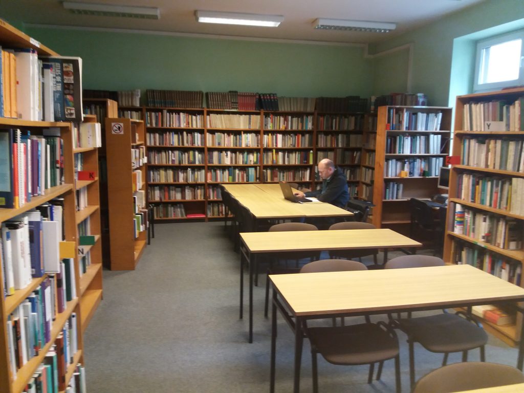 Regały biblioteczne, stoliki, przy stoliku czytelnik pracujący z własnym laptopem