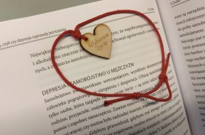 Zdjęcie wisiorka w kształcie serca - Wybieram-życie. W tle strona książki.