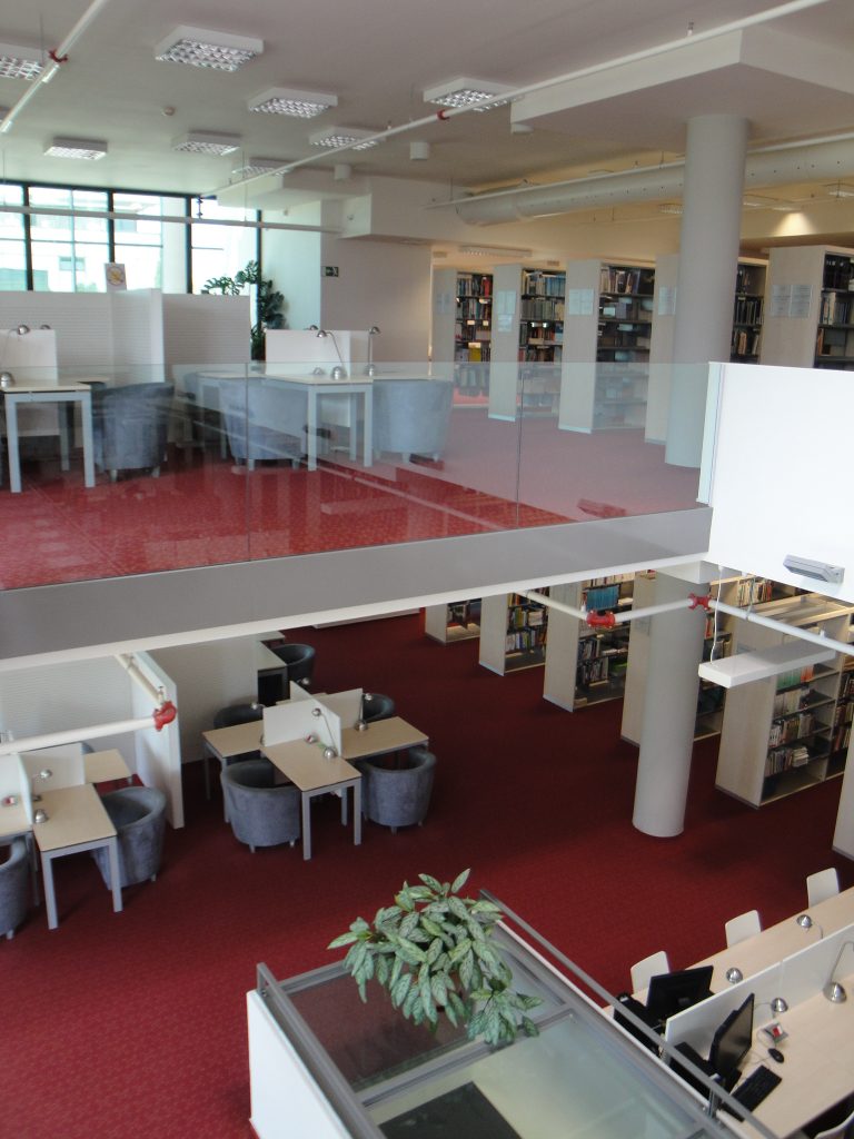 Zdjęcie przestrzeni bibliotecznej z regałami z książkami oraz miejscami pracy dla użytkowników.
