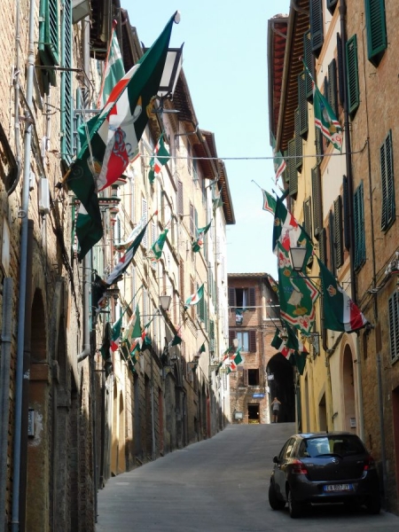 Ulica w Sienie. Na ulicy zaparkowany samochód, w oknach wywieszone flagi.