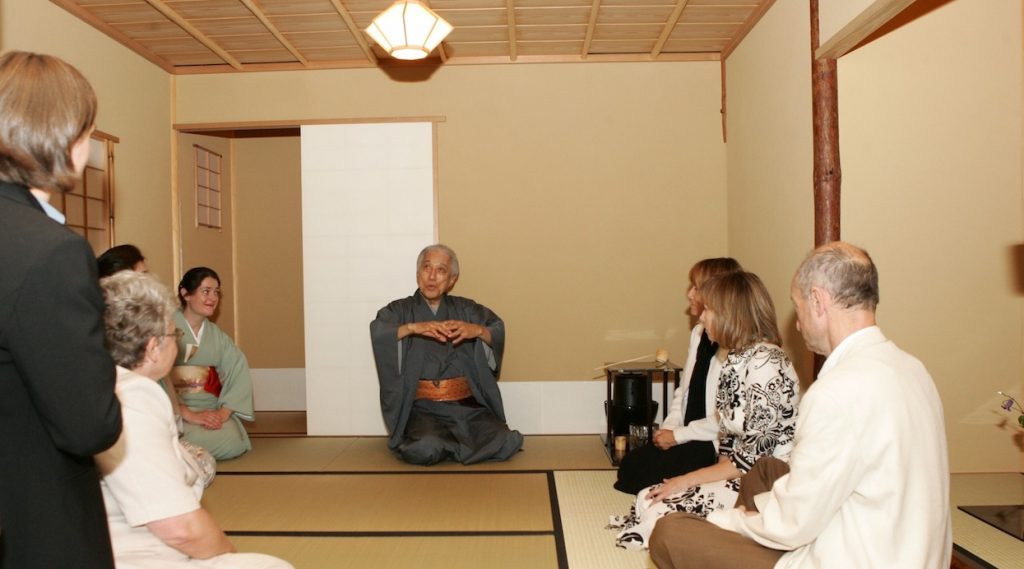 Zdjęcie kilku osób słuchających wykładu starszego mężczyzny w tradycyjnym stroju japońskim