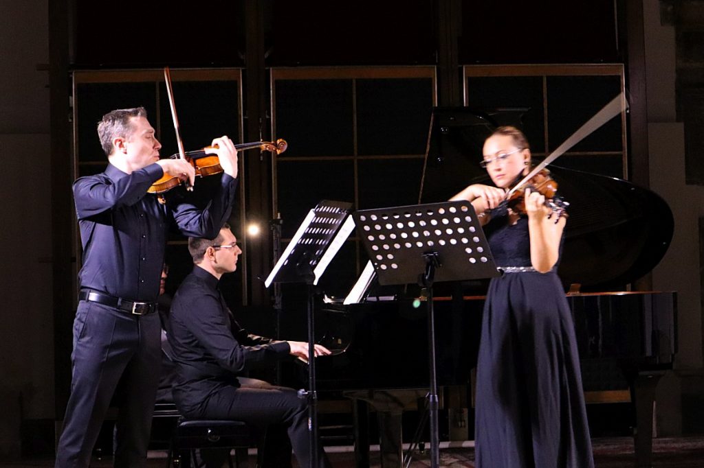Grupa ludzi grająca na skrzypcach. Dwóch mężczyzn i jedna kobieta.