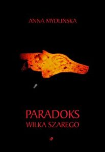 Okładka książki Paradoks wilka szarego, czarne tło i zarys głowy wilka w odcieniach żółtych i pomrańczowych