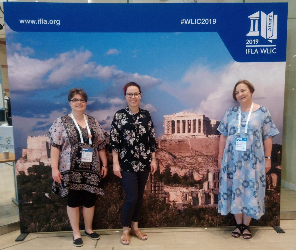 Zdjęcie trzech bibliotekarek przed banerem konferencji IFLA