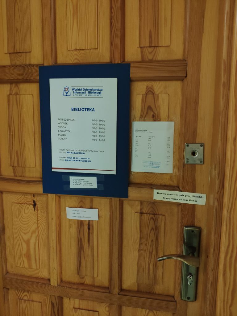Drewniane drzwi z informacją o godzinach otwarcia biblioteki