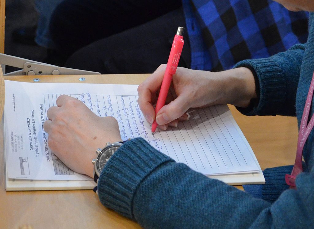Dłonie nad arkuszem papieru, w prawej różowy długopis.