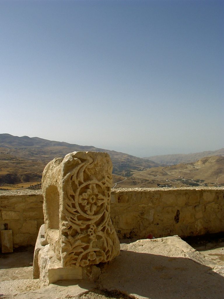 kamień z płaskorzeźbą, fragment muru i widok na wzgórza
