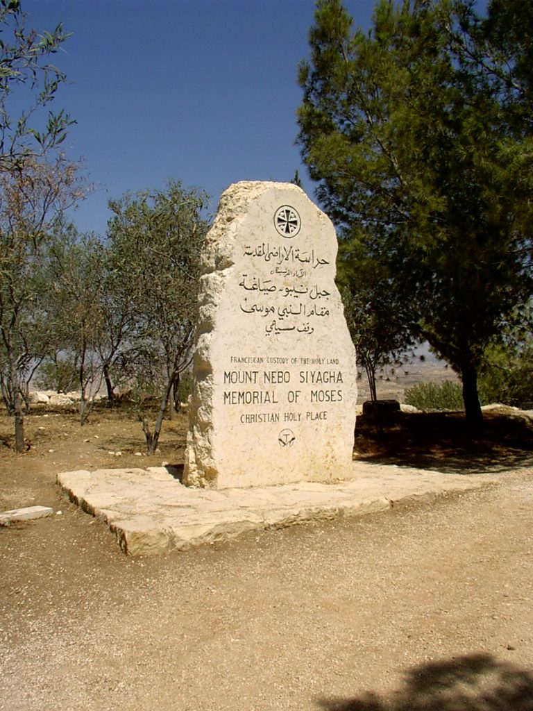 Obelisk z napisami w języku arabskim i angielskim, w tle drzewa oliwkowe.