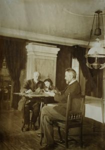 Fotografia pokoju, w którym dwaj starci panowie oraz chłopiec grają w karty