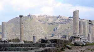 Zdjęcie. Na pierwszym planie ruiny kolumnady. w tle wzgórze z ruinami.
