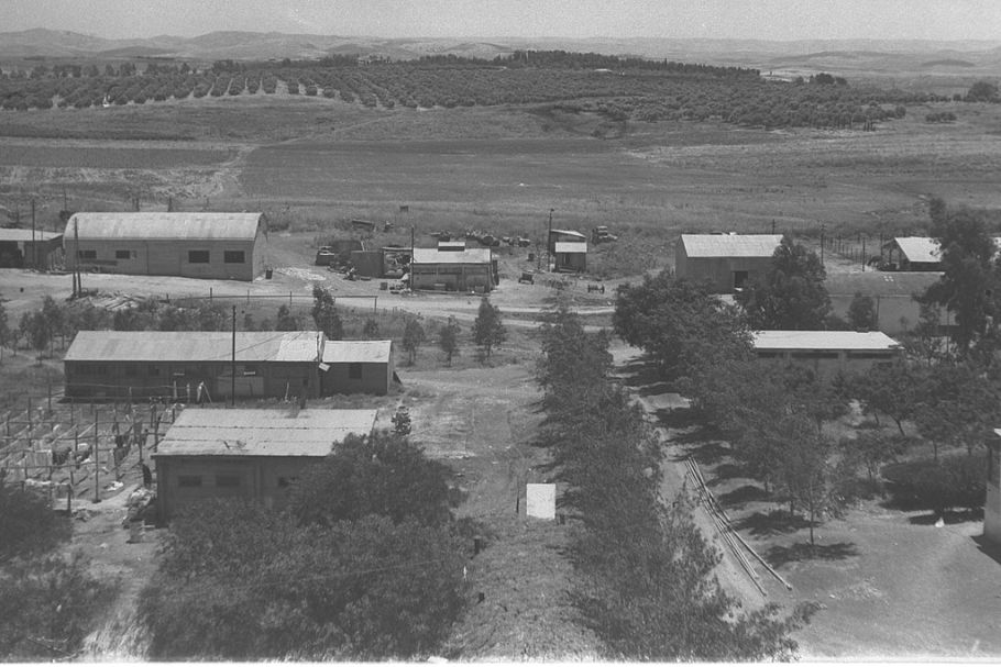 Czarno-białe zdjęcie parterowych budynków. Na dalszym planie widać sad na wzgórzach.