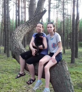 dwie kobiety i czarny pies siedzą na wygiętej sośnie, drzewo