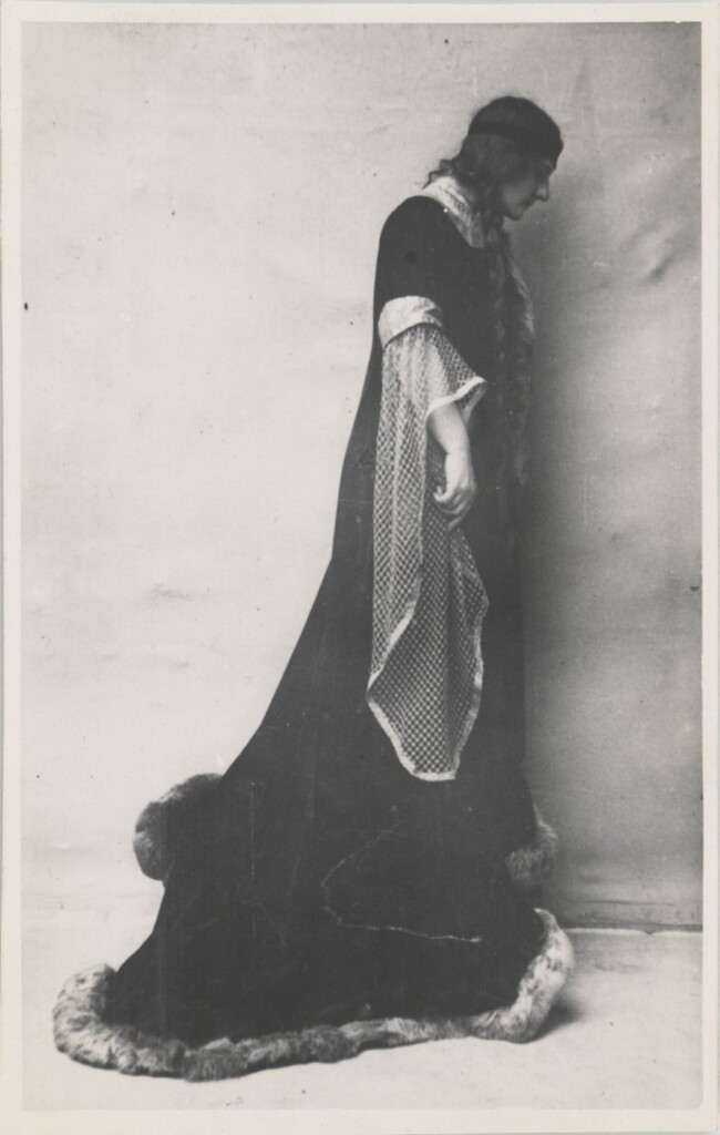 kobieta uczesana w dwa długie warkocze ubrana w długi do ziemi płaszcz podbity futrem