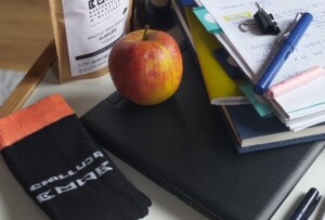 Zdjęcie fragmentu stołu ze stosem notatników, kawą, jabłkiem i skarpetką