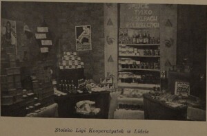 Zdjęcie podpisane: stoisko Ligi Kooperatystek w Lidzie. Wystawa przedstawiająca produkty z oferty sklepu ustawione na półkach i poukładane w piramidy. Na ścianie dwa plakaty i dwa hasła: czystość, porządek, [niewyraźny napis] Społem oraz [k]upujcie tylko w sklepach spółdzielczych.