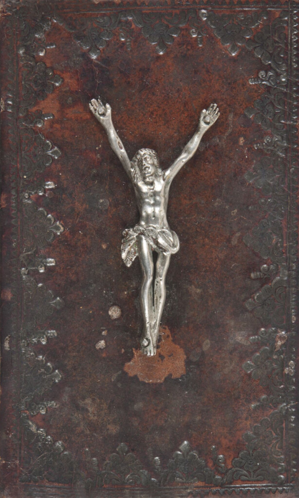 Zdjęcie okładki ksiązki, do które przymocowana jest metalowa figurka ukrzyżowanego Chrystusa