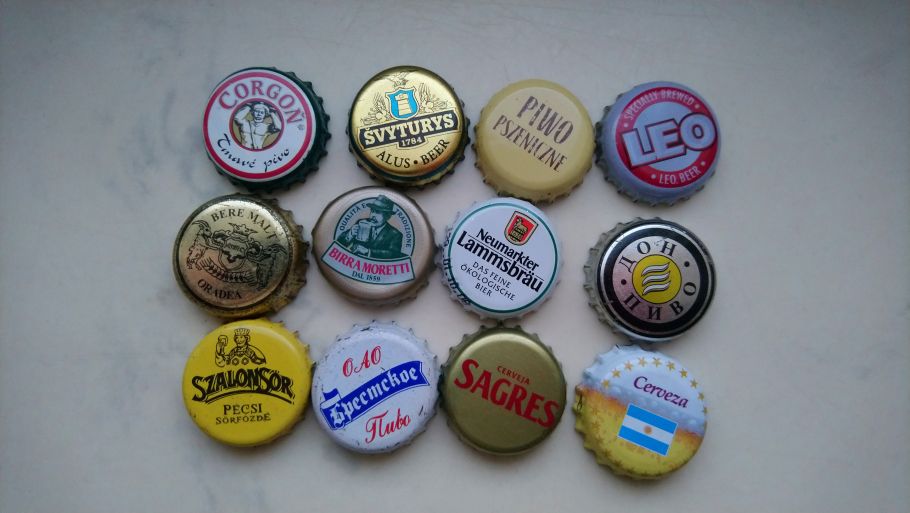 Zdjęcie kilkunastu różnokolorowych kapsli od piwa ułożonych na jasnym tle