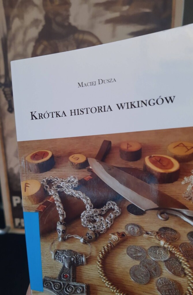 Okładka książki Krótka Historia Wikingów, na niej zdjęcie rozłożonych na stole monet, kosztowności , run i noża.