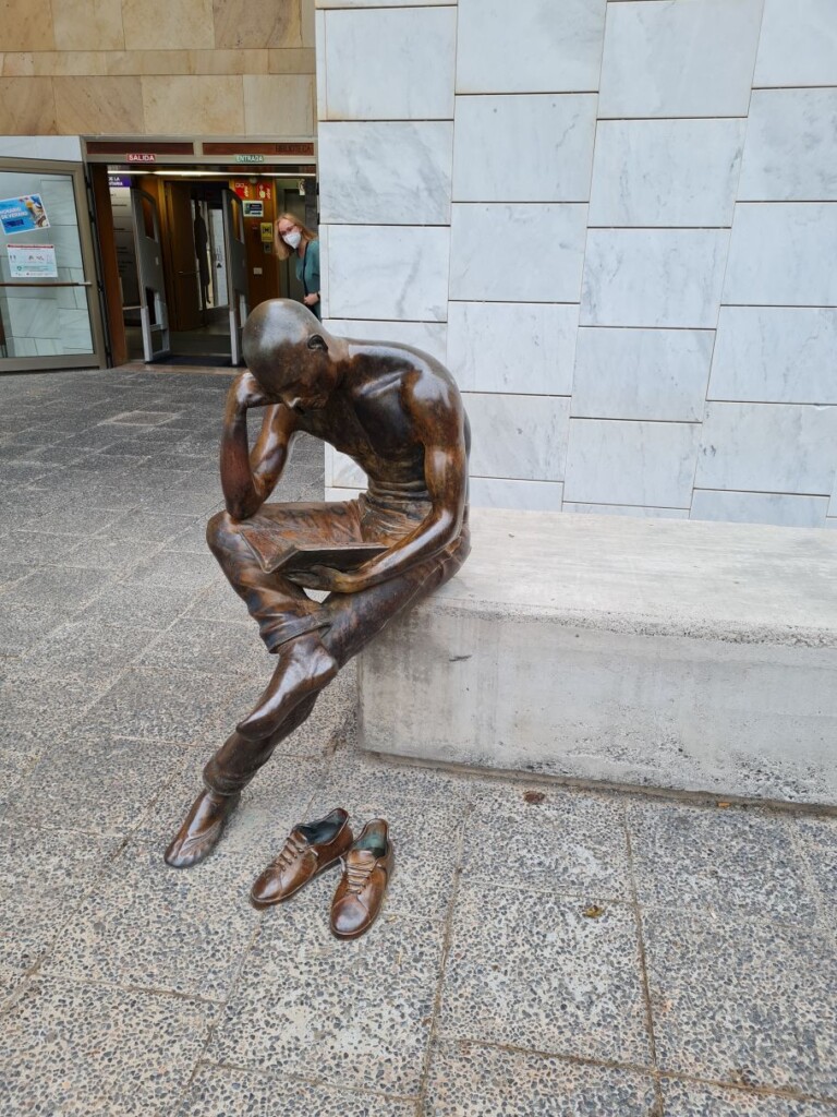 rzeźba czytającego młodzieńca siedzącego na murku przed wejściem do budynku