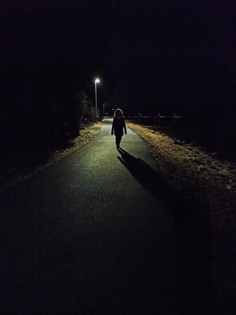 postać idąca nocą po drodze oświetlonej latarniami