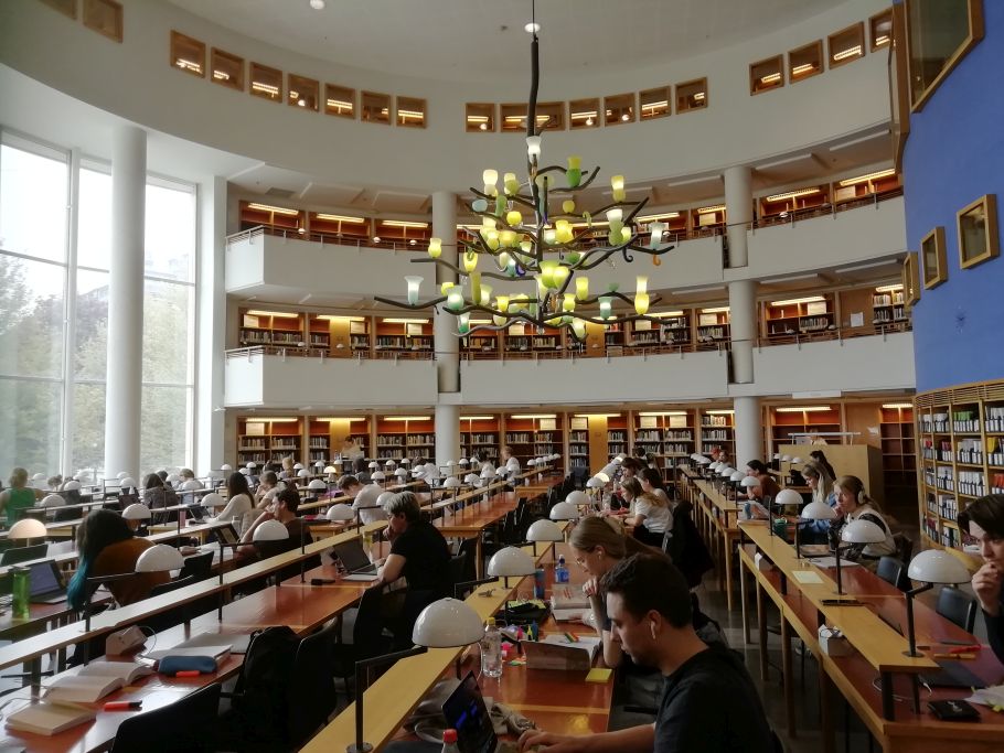 czytelnia biblioteczna wypełniona ludźmi, w centrum zdjęcia piękny żyrandol