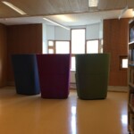 Zdjęcie przestrzeni bibliotecznej, ustawione przy oknie kolorowe fotele.