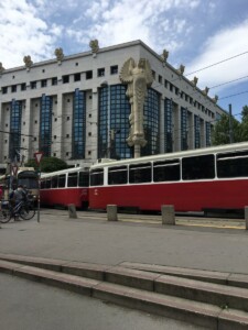 Zdjęcie budynku biblioteki z charakterystyczną rzeźbą sowy na fasadzie, na pierwszym planie przejeżdżające tramwaje.