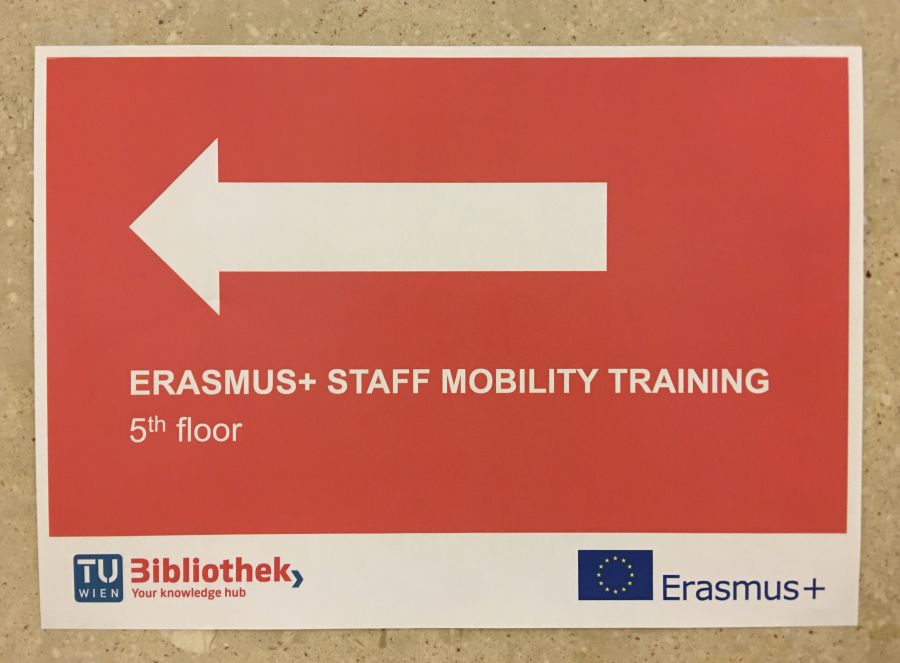 Zdjęcie kartki, na czerwonym tle biała strzałka w lewo i napis Erasmus+ Staff Mobility Training 5th floor.