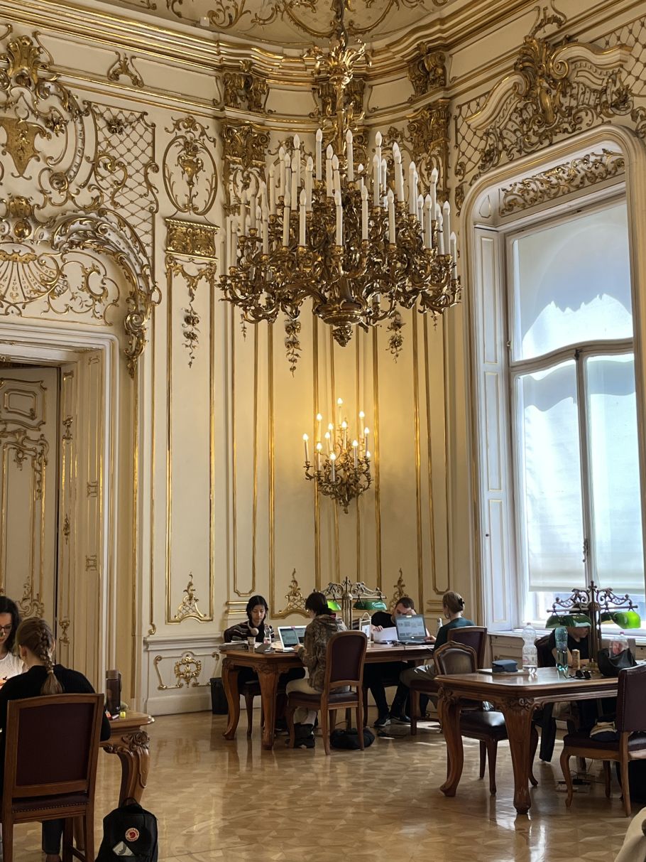 ludzie czytają przy stołach w barokowym wnętrzu