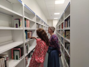 Dwie kobiety przyglądają się książkom na półce na regale bibliotecznym.