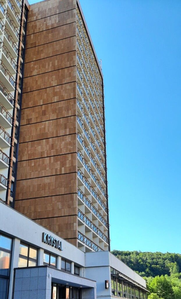 Zdjęcie wysokiego budynku, fasadę stanowią balkony, nad wejściem napis Krystal